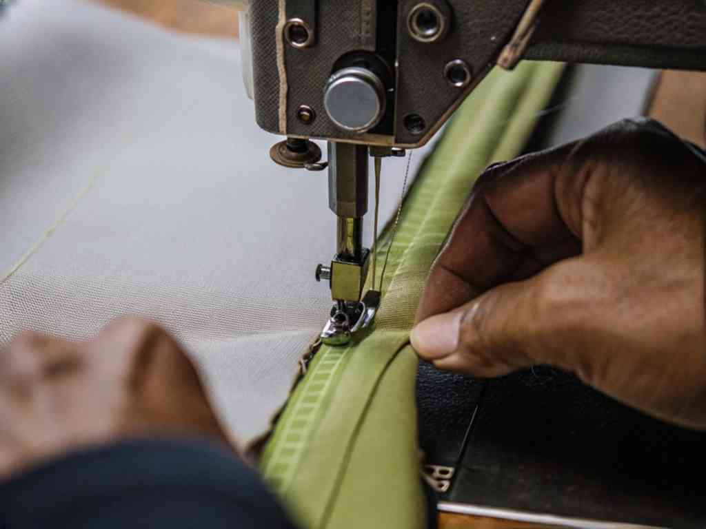 Hands guiding green fabric through industrial sewing machine
