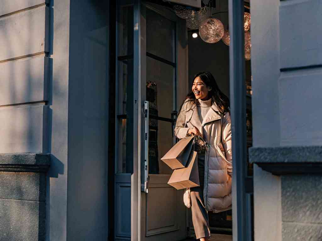 A woman exiting a store with shopping bags and a smile.