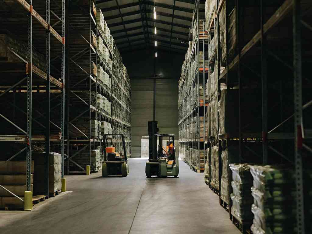 A forklift moving goods in a large warehouse with tall storage racks.