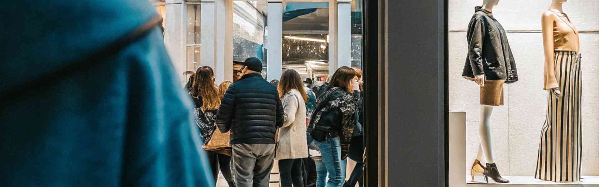 People passing by a fashion store window displaying stylish mannequins.