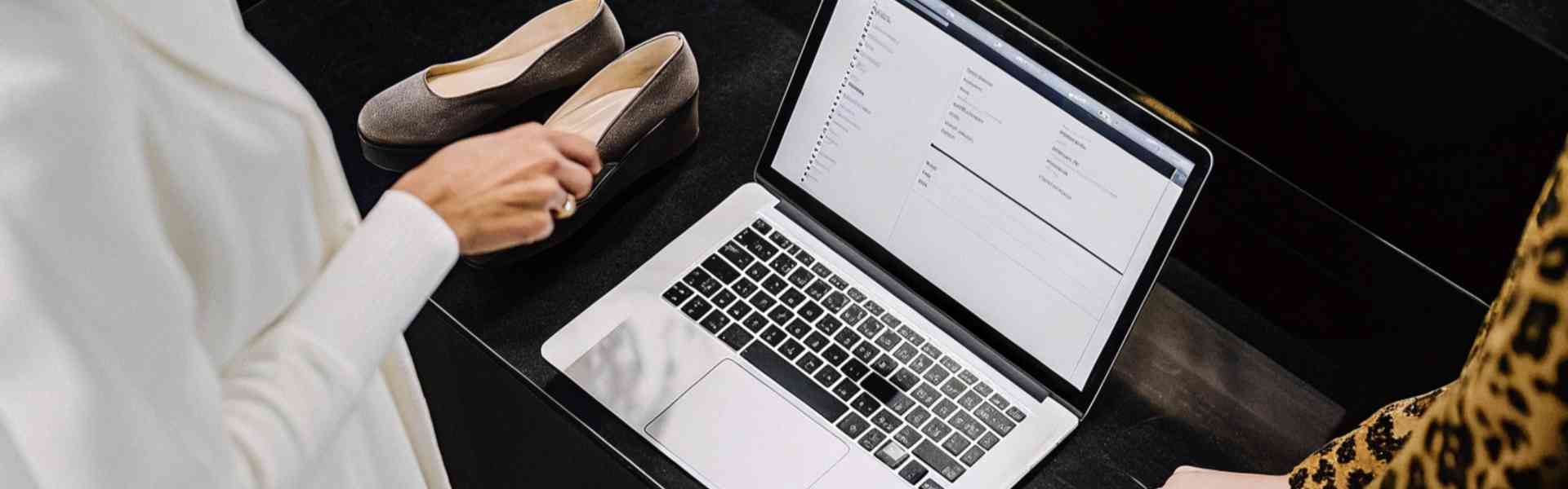 Two women using a laptop in a boutique, with shoes on display.