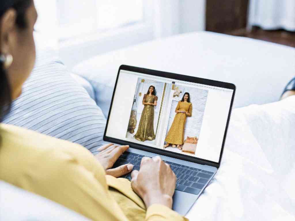 A woman browsing dresses on a laptop while relaxing on a couch.