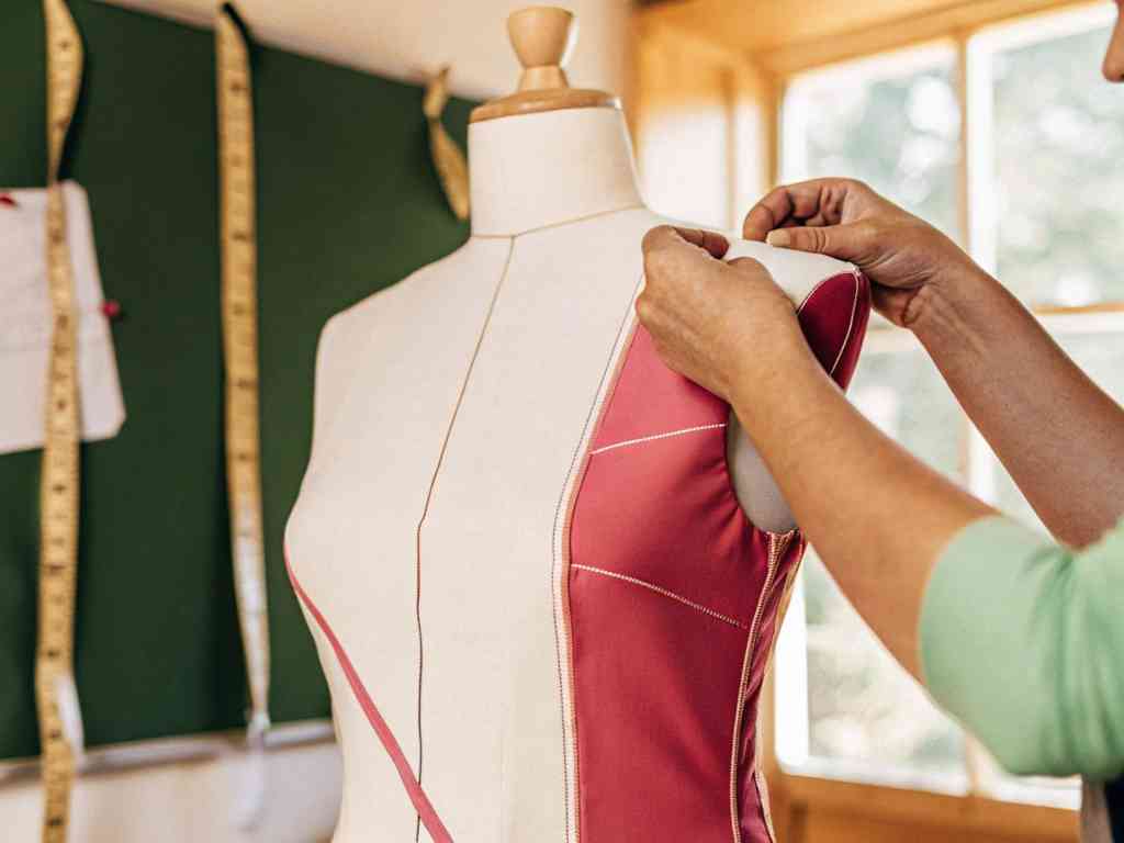 Designer working on pink dress fitting on mannequin.