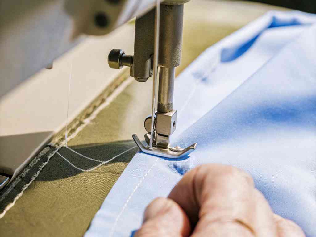 A sewing machine stitching a light blue fabric with a guiding hand.