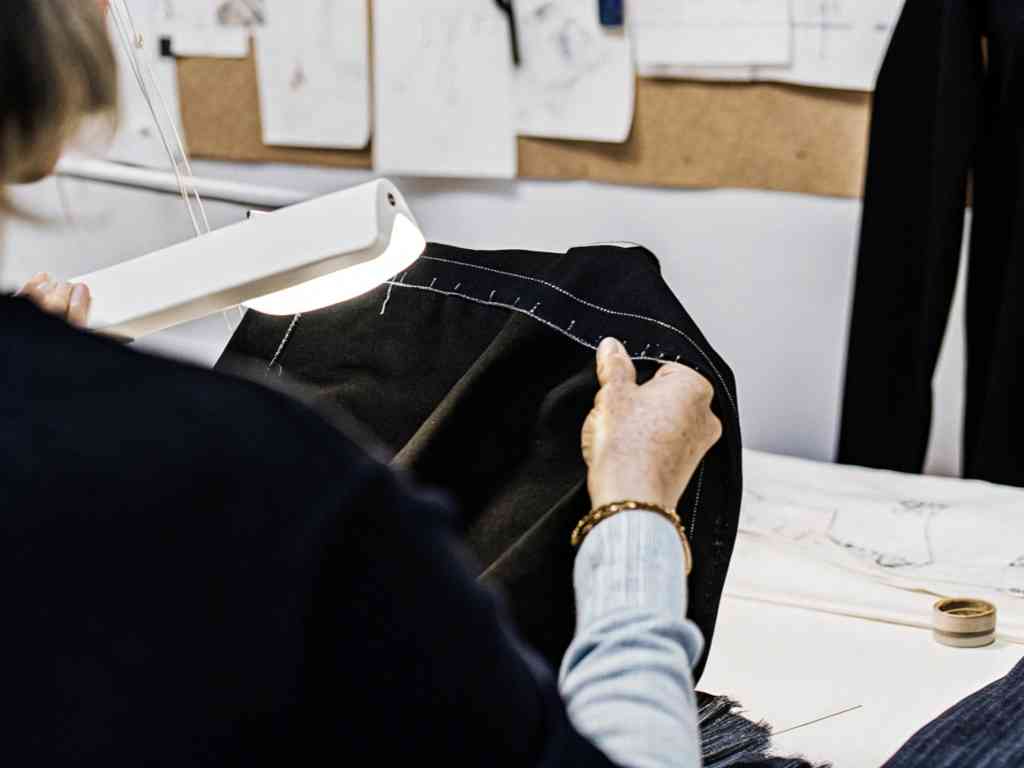 Designer stitches black fabric under work light.