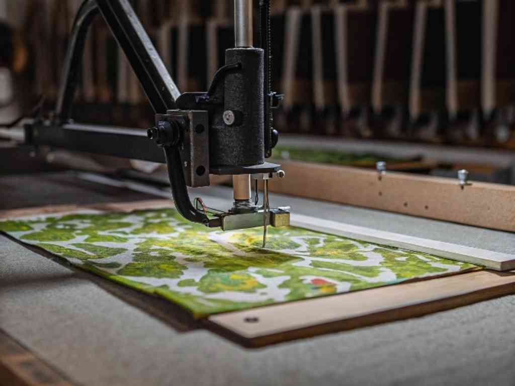 An industrial embroidery machine stitching a green fabric design.