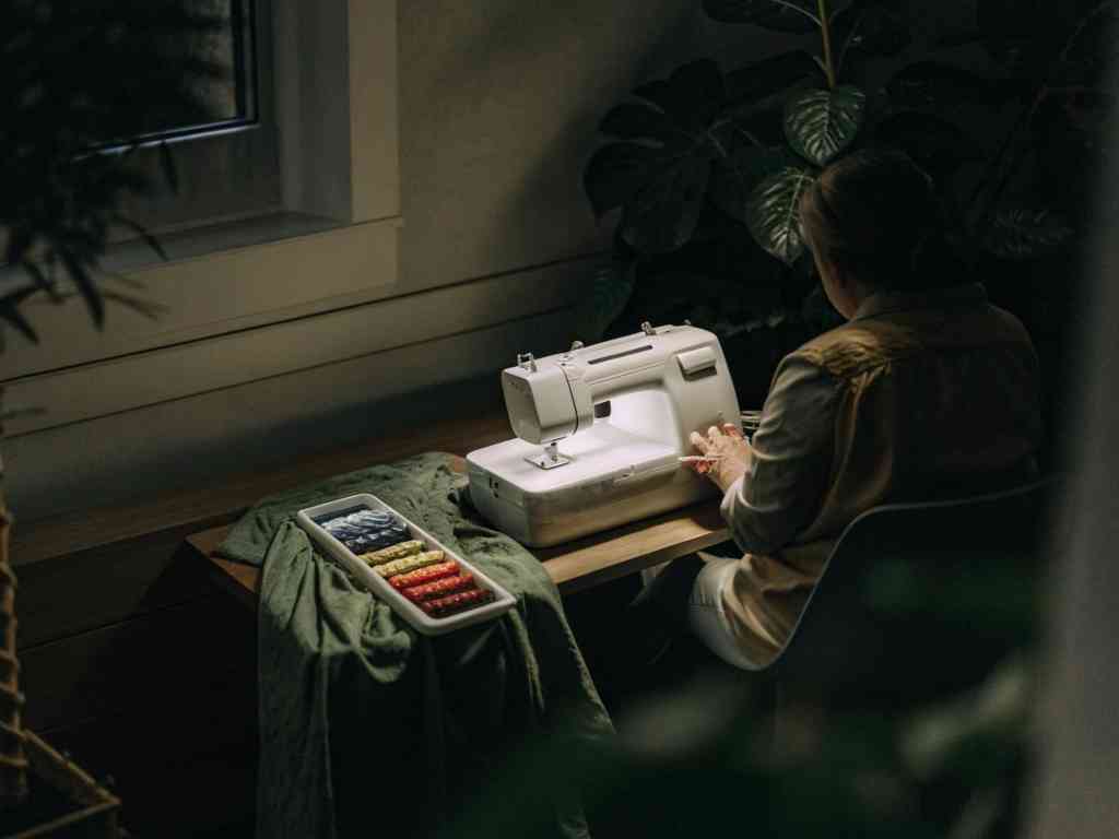 A woman sewing at a wooden table with a sewing machine, fabric, and colorful thread.