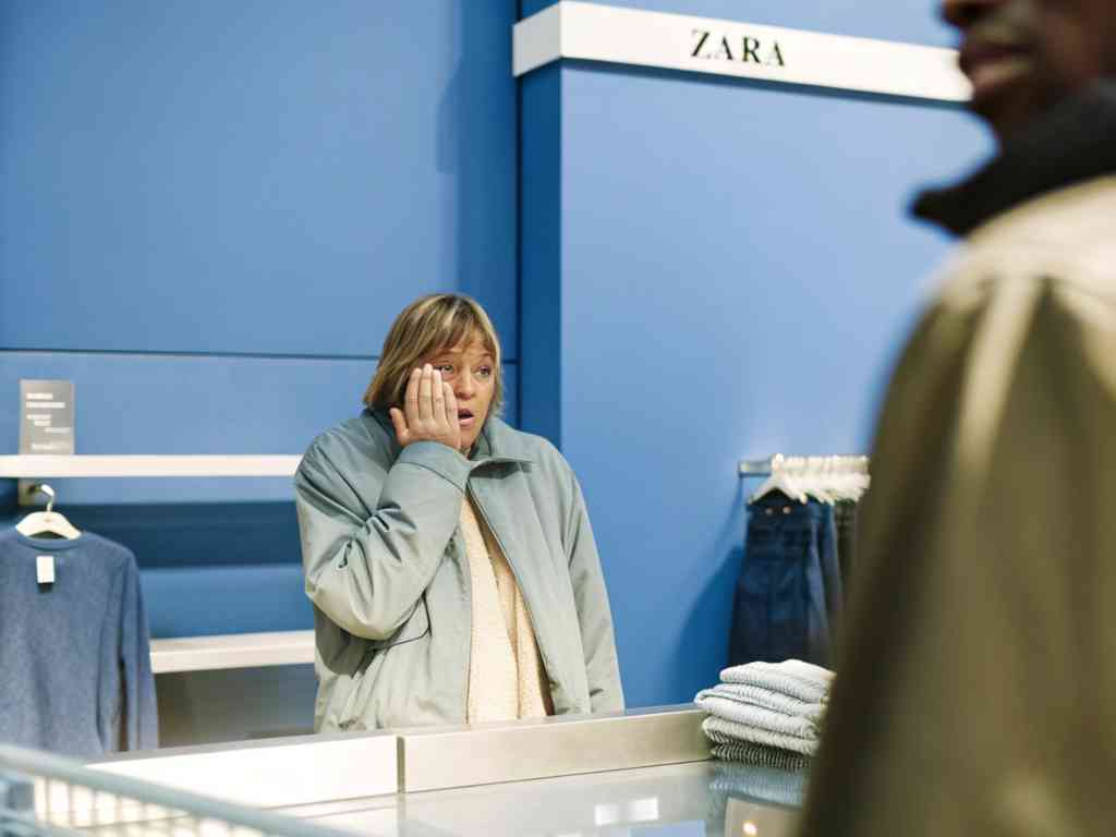 A surprised woman in a Zara store covering her face with one hand.