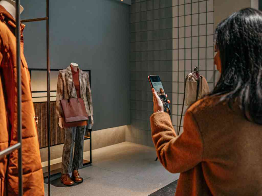 Woman taking a photo of a stylish mannequin display in a clothing store.