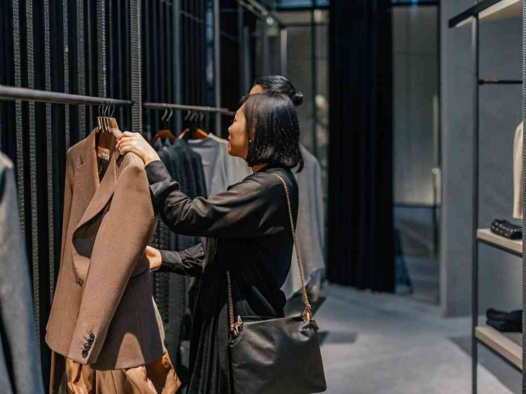 A woman in a black outfit shopping for a brown blazer in a stylish clothing store.