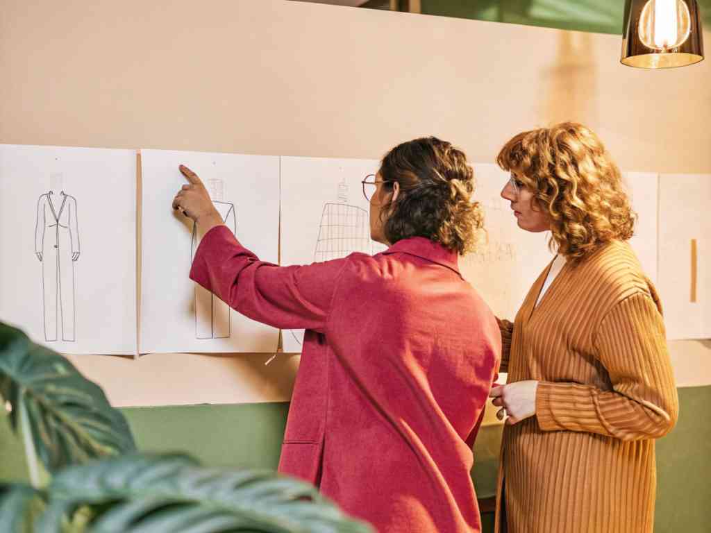 Designers pointing at garment sketches on wall.