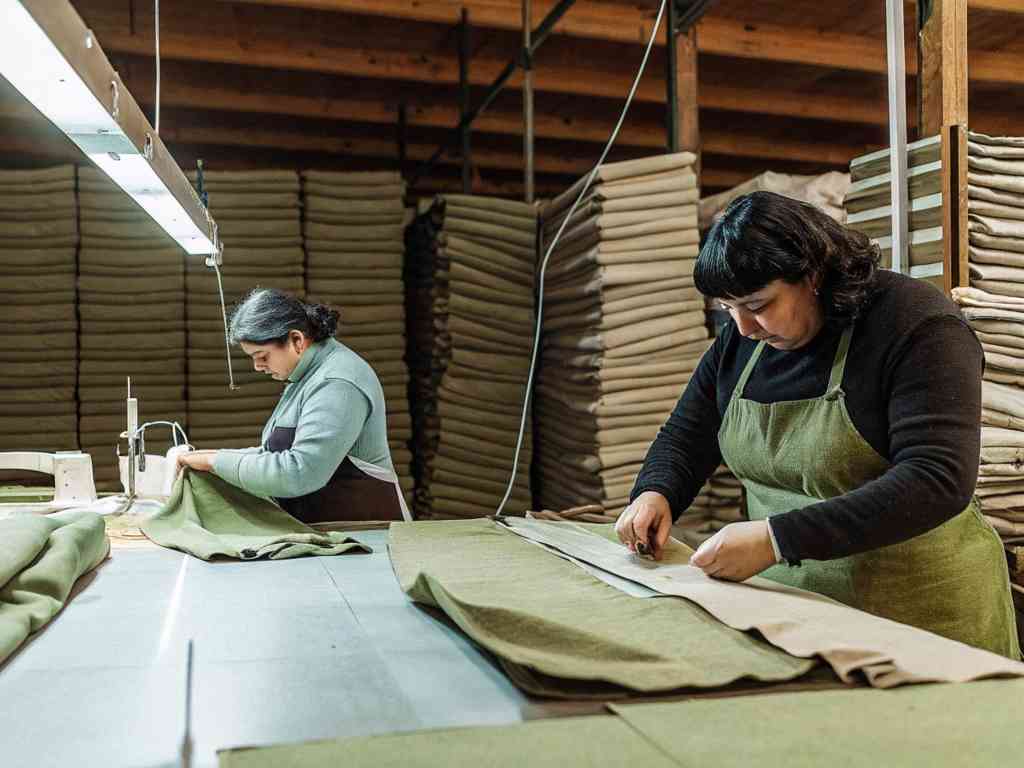 Two women in aprons cutting and sewing green fabric in a textile workshop.