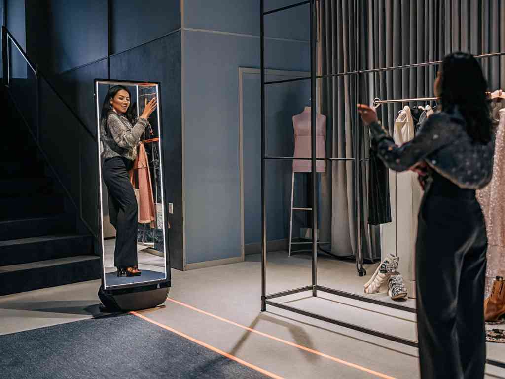 Two women using a smart mirror in a modern fashion boutique.