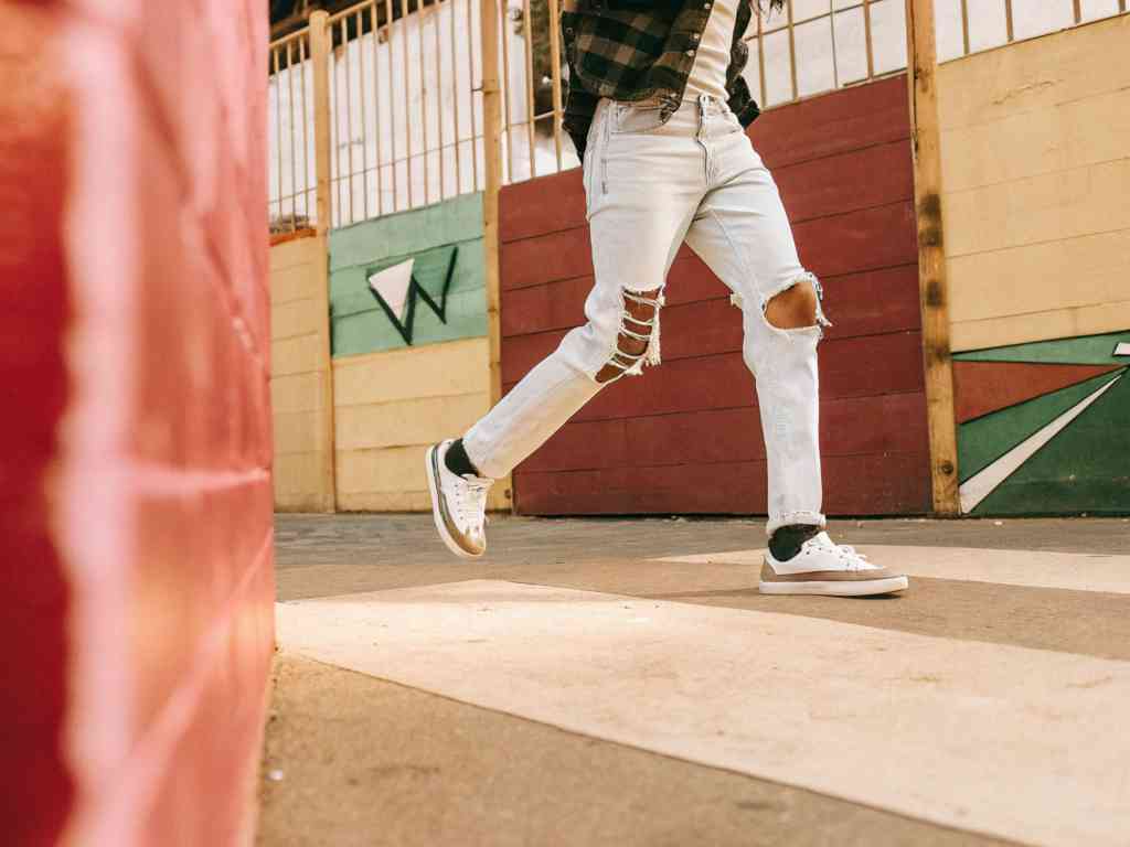Person wearing ripped light-wash jeans and white sneakers