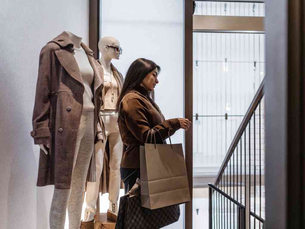 A woman shopping in a boutique with mannequins in elegant outfits.