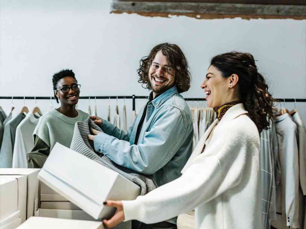Three people packing sweaters in fashion studio.