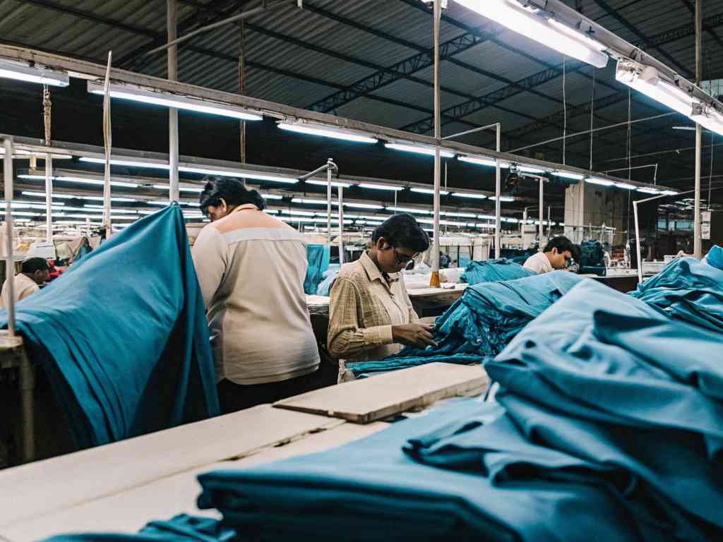 Workers handling and inspecting blue fabric in a busy garment factory.