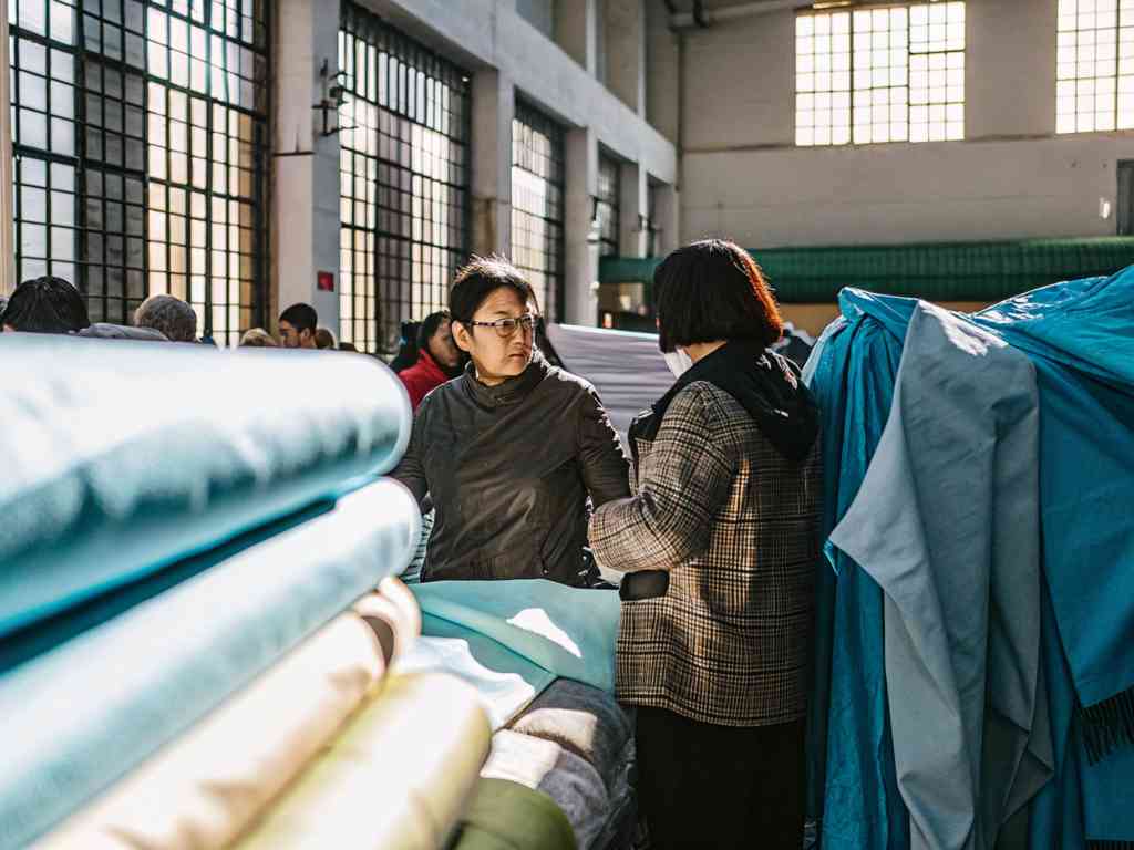 Two women discussing fabric selection in a sunlit textile market.