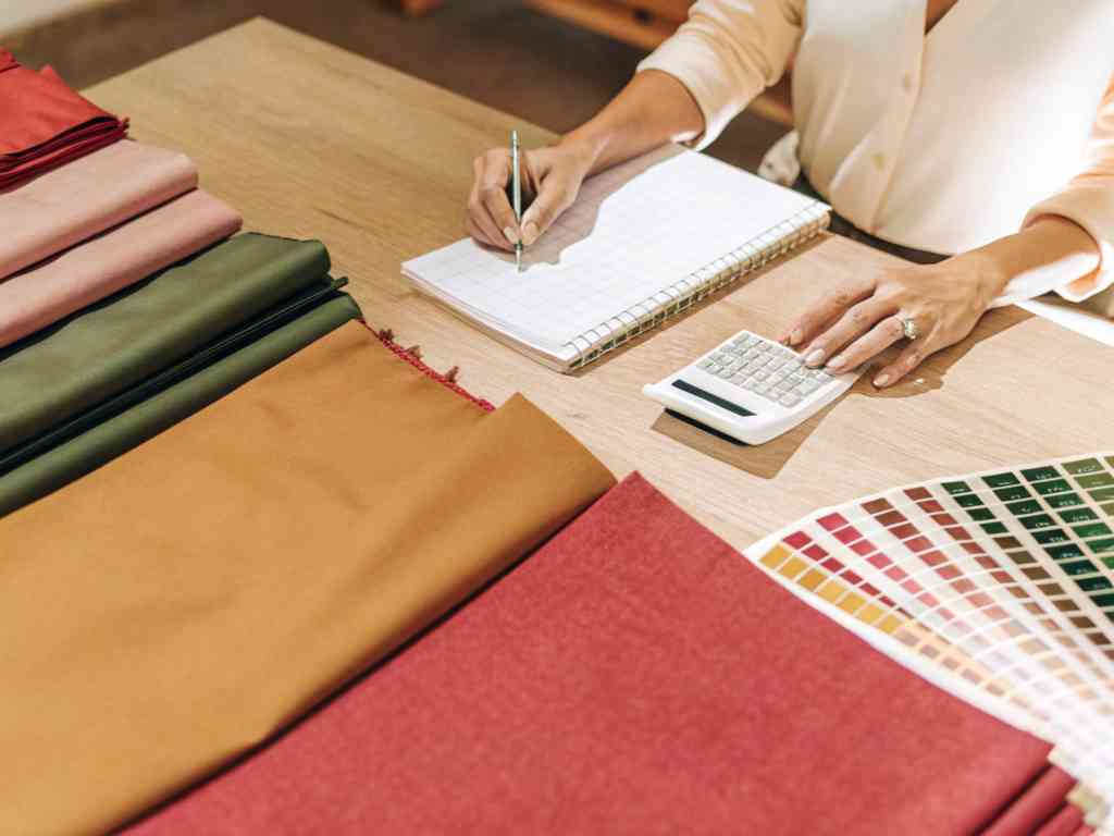 A person calculating fabric costs with samples and a color chart.