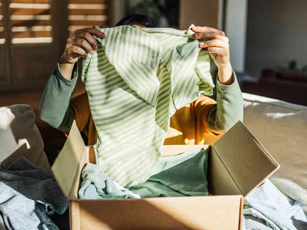 A person unpacking a green striped garment from a cardboard box.