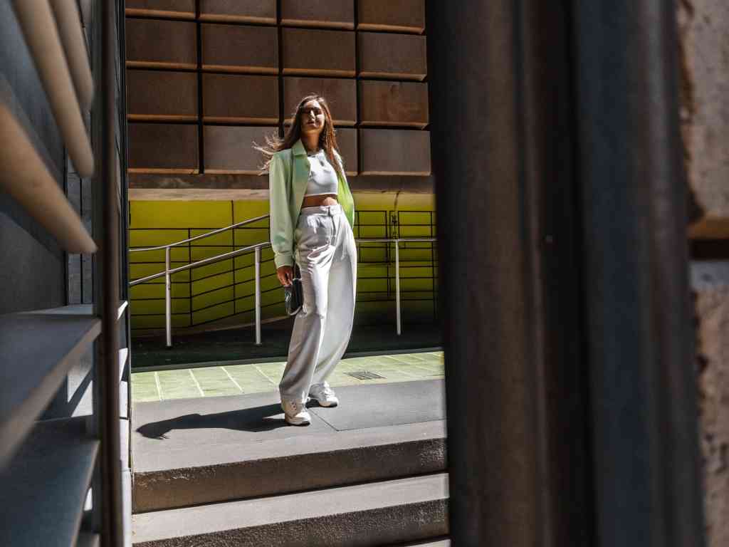 A stylish woman in a cropped top, blazer, and wide-leg pants walks confidently in an urban setting.