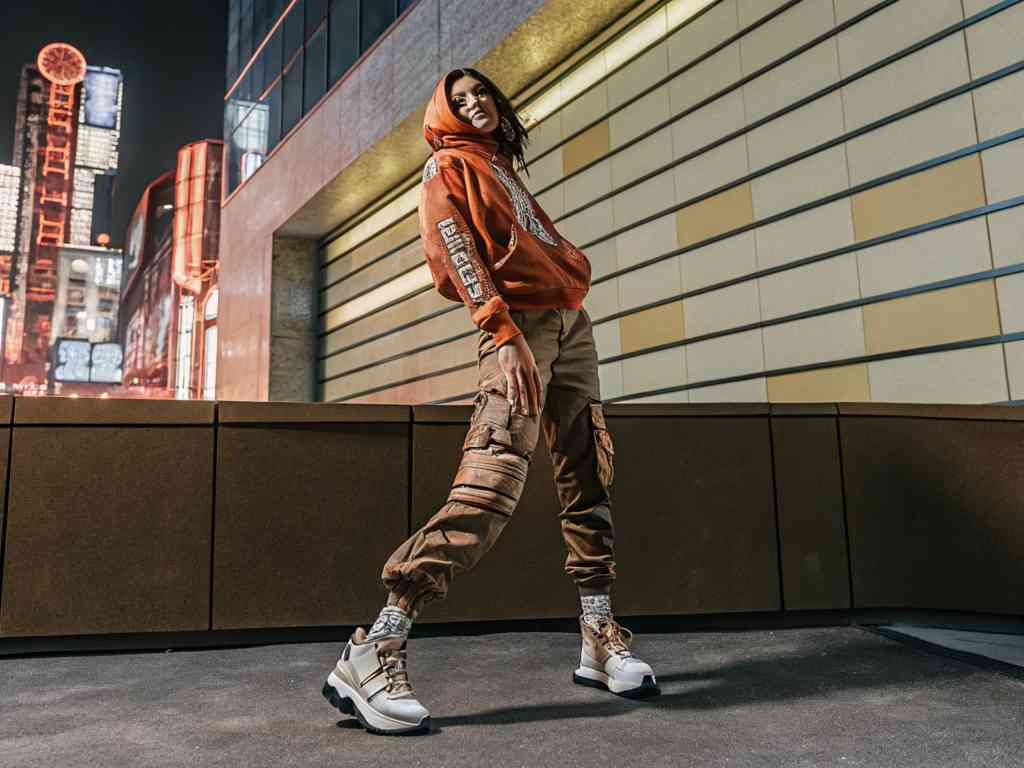 Stylish woman in cargo pants and hoodie posing in a city at night.