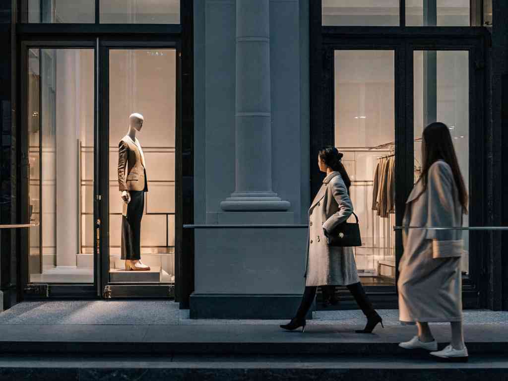 Two stylish women walking past a fashion boutique window display.