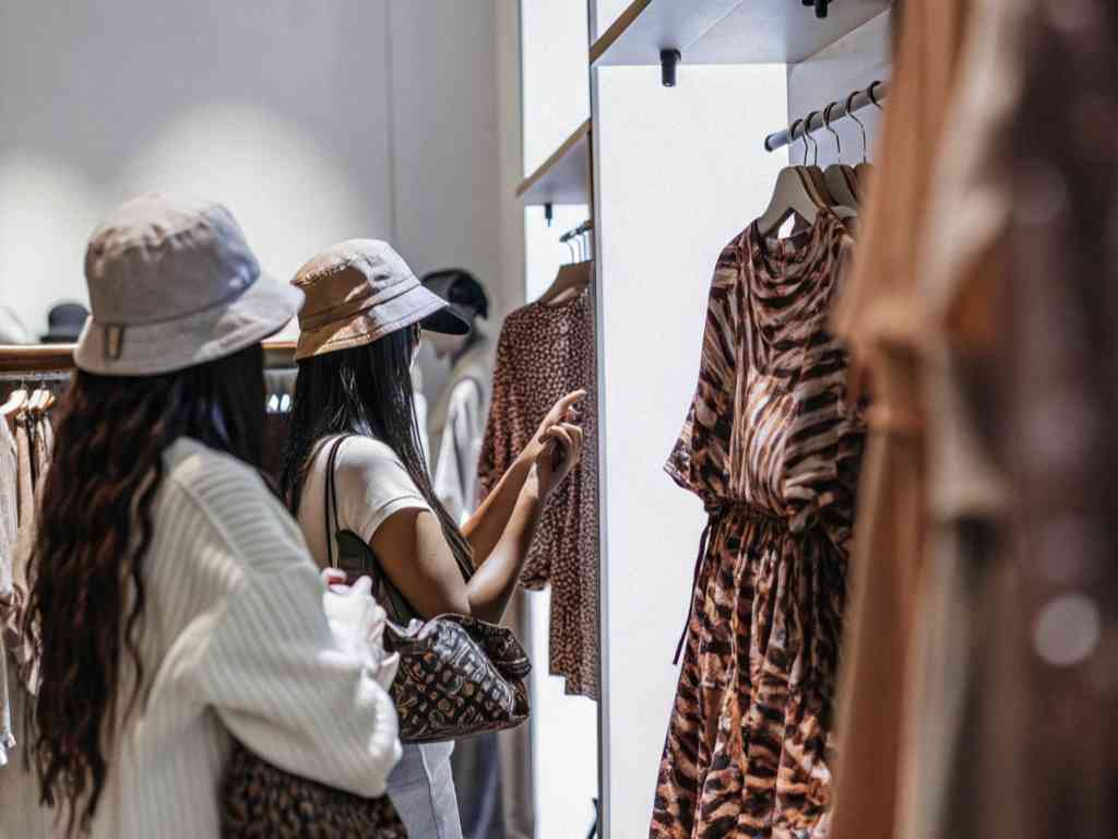 Two women shopping and examining printed dresses in a boutique