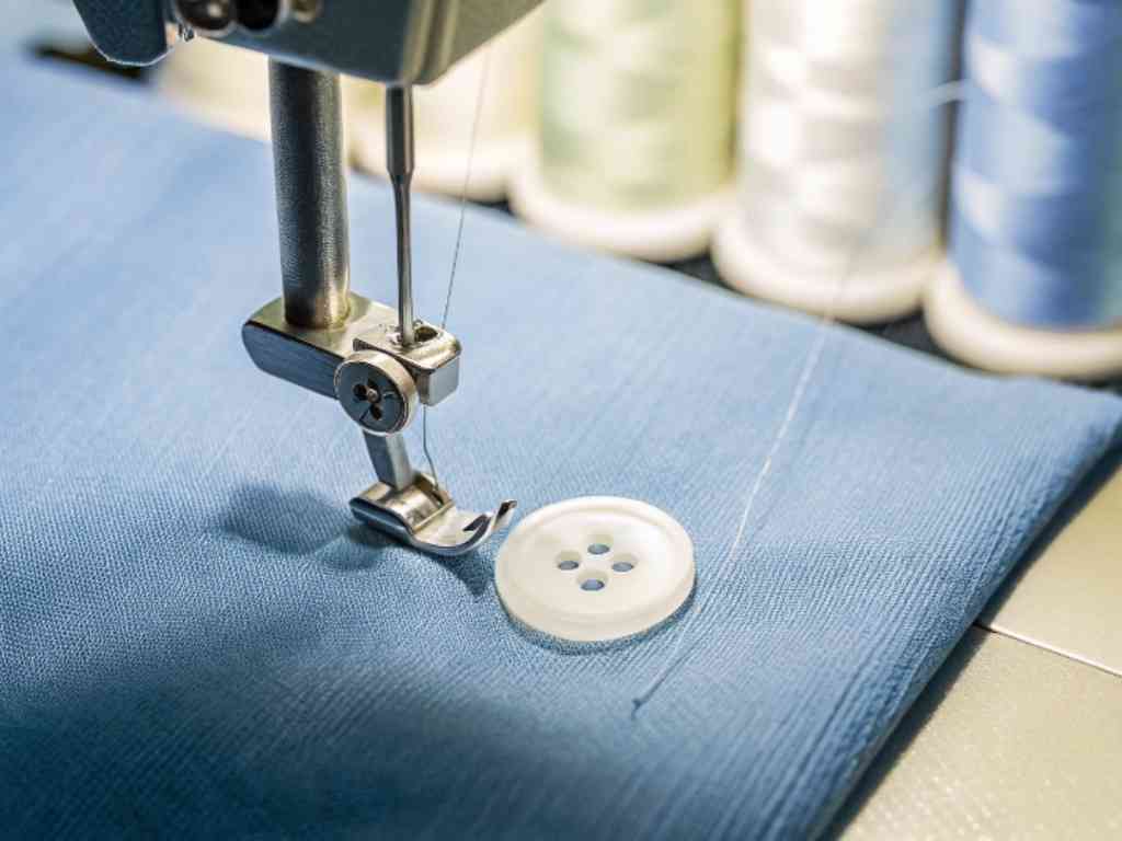 Sewing machine needle above button on blue textile material.