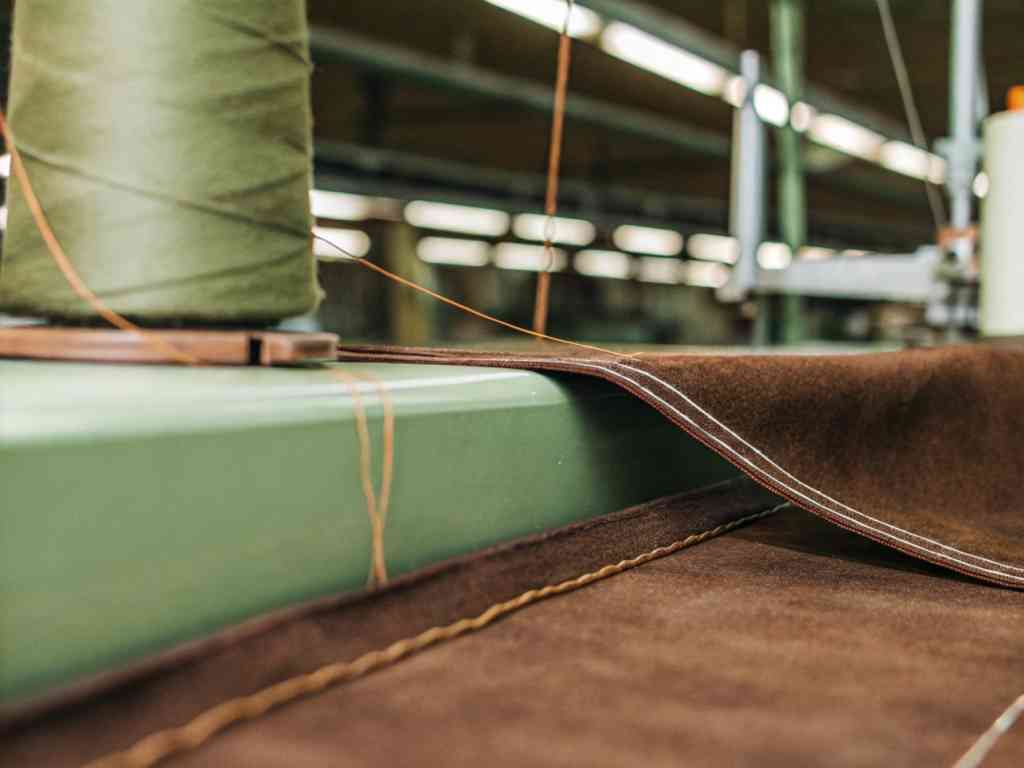 Industrial sewing machine stitching brown fabric with green thread