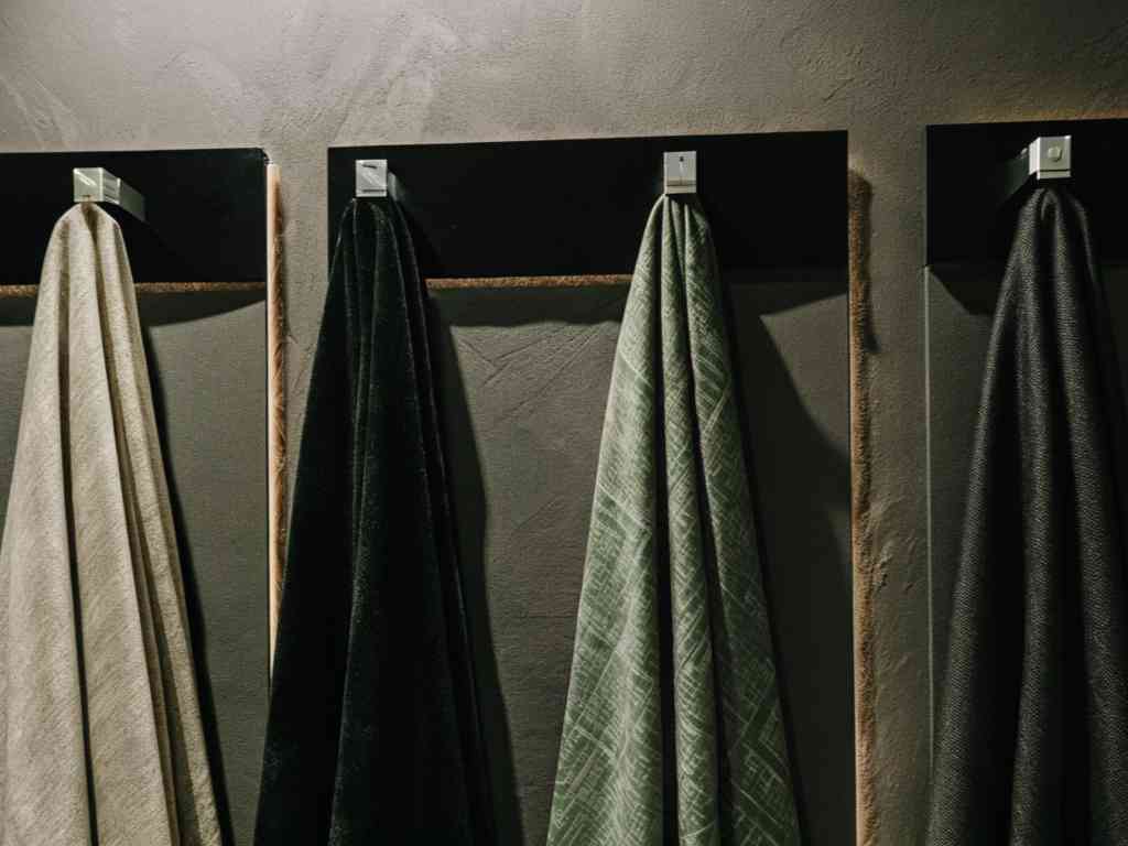 Hanging fabric samples in neutral and green tones on display wall