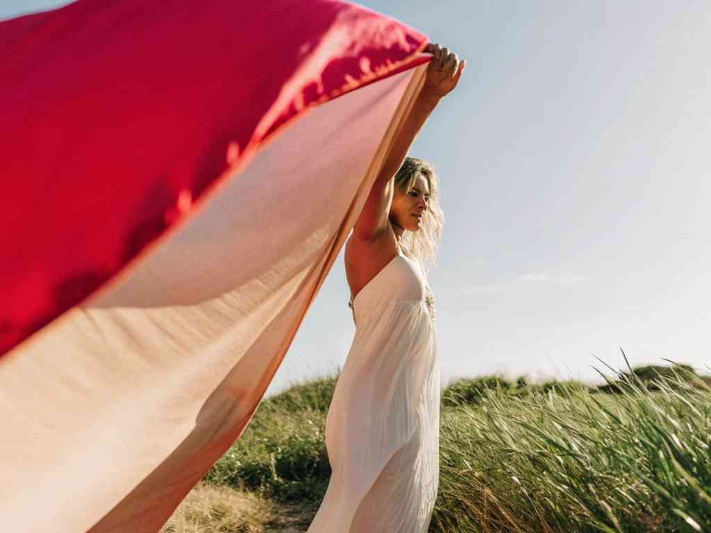 Woman holding a large red and white fabric on a grassy field