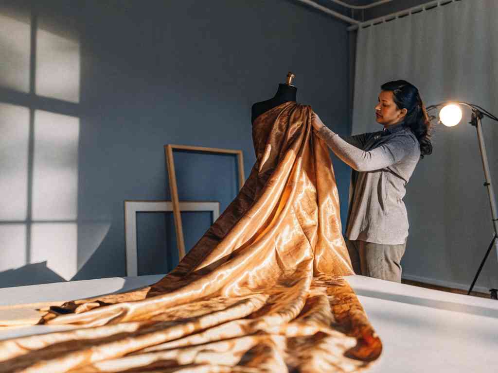 Designer adjusting luxurious gold fabric on a black mannequin in a creative workspace.