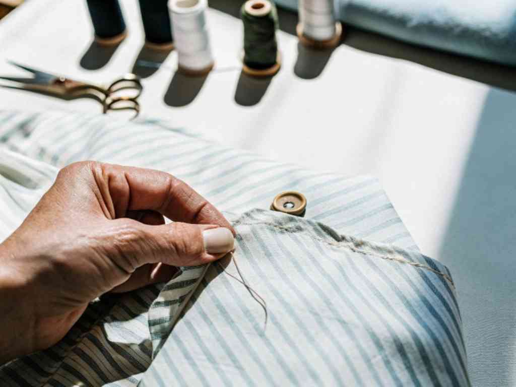Hand stitching button on striped fabric under bright studio light.