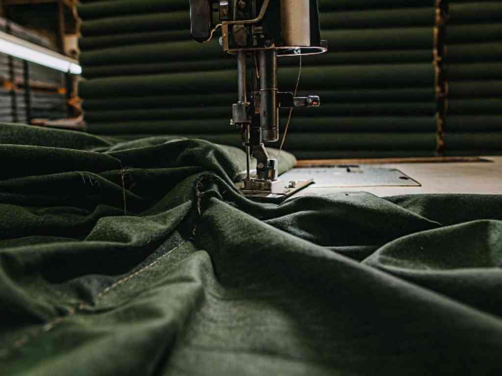 Dark green fabric being sewn in factory with fabric rolls.