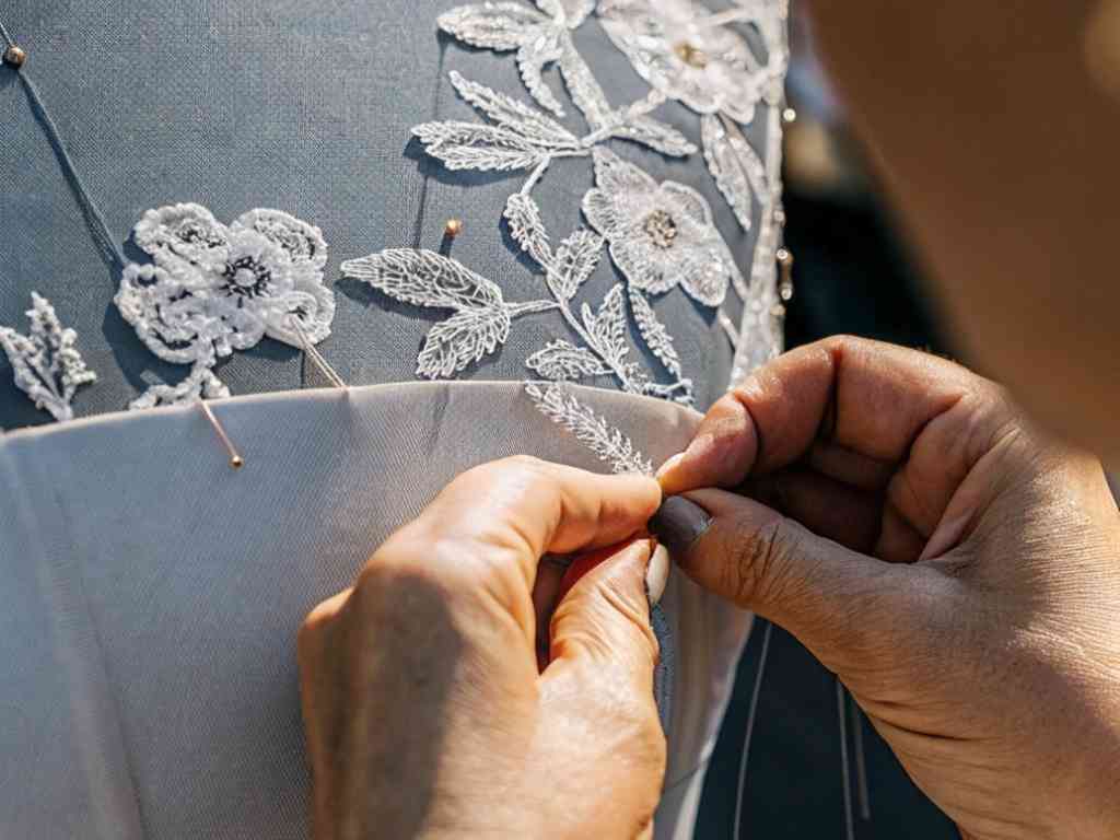 Hands stitching floral lace applique onto a dress bodice.
