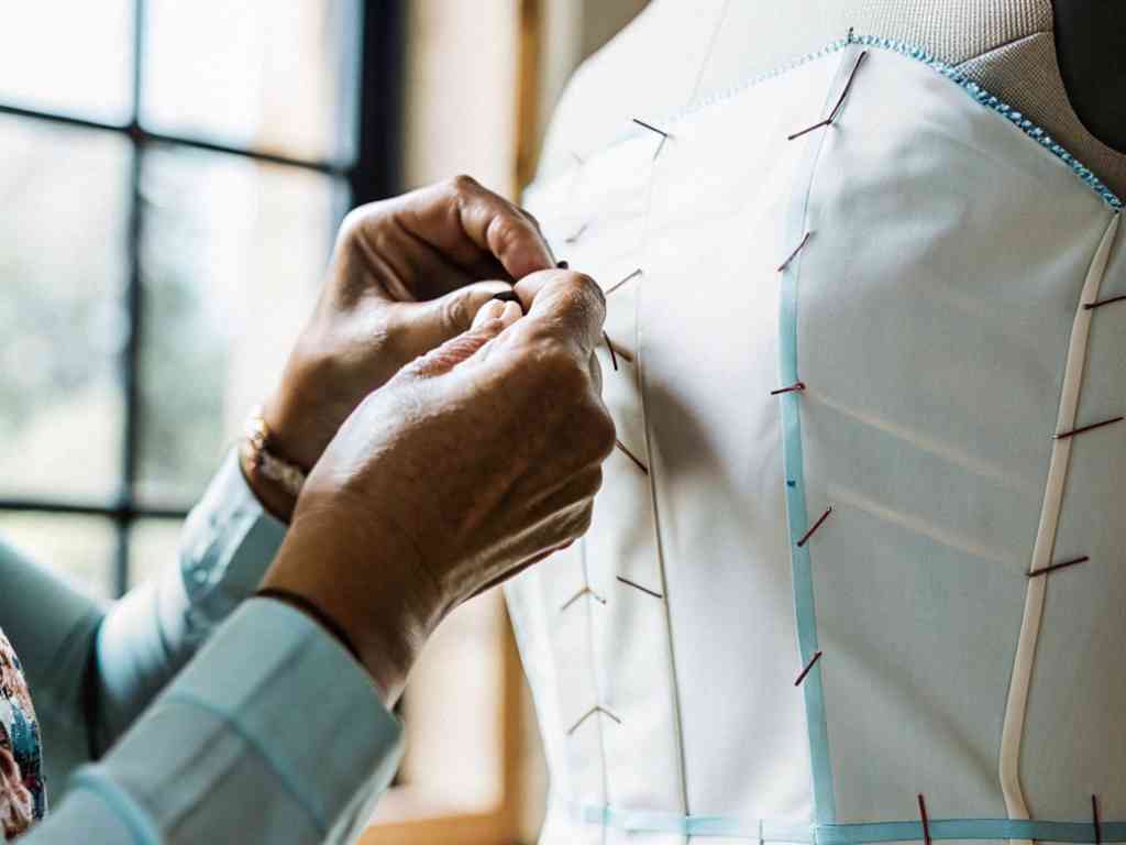 Close-up of hands pinning a white muslin bodice on a dress form.