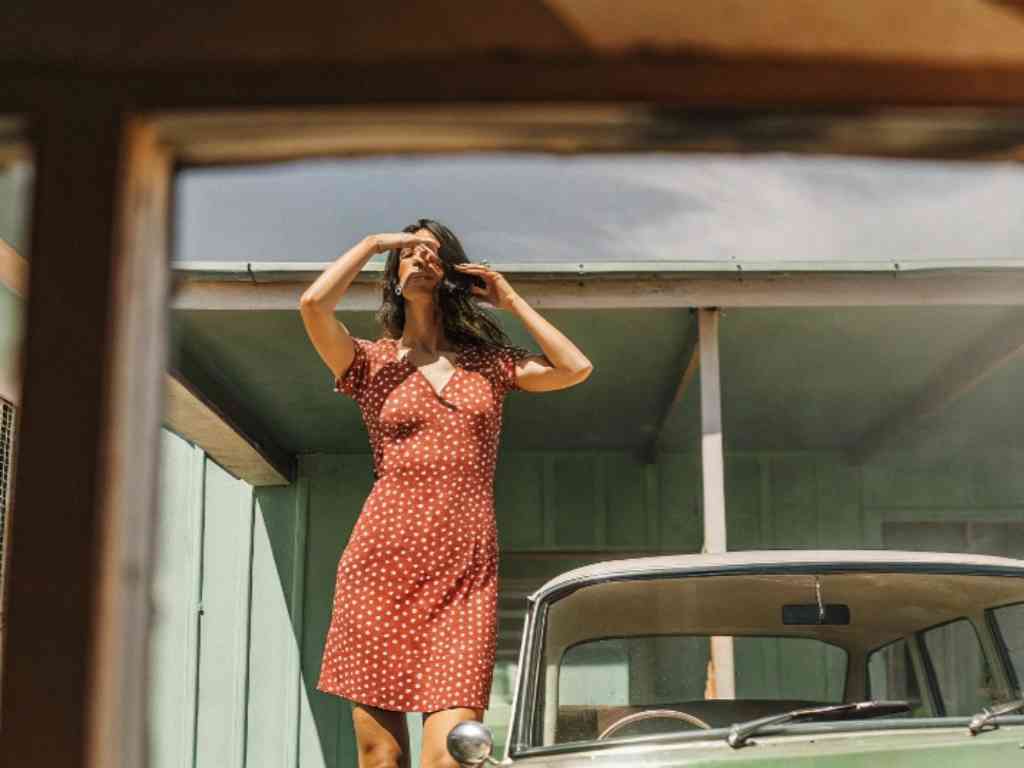 Woman in red polka dot dress standing beside vintage car