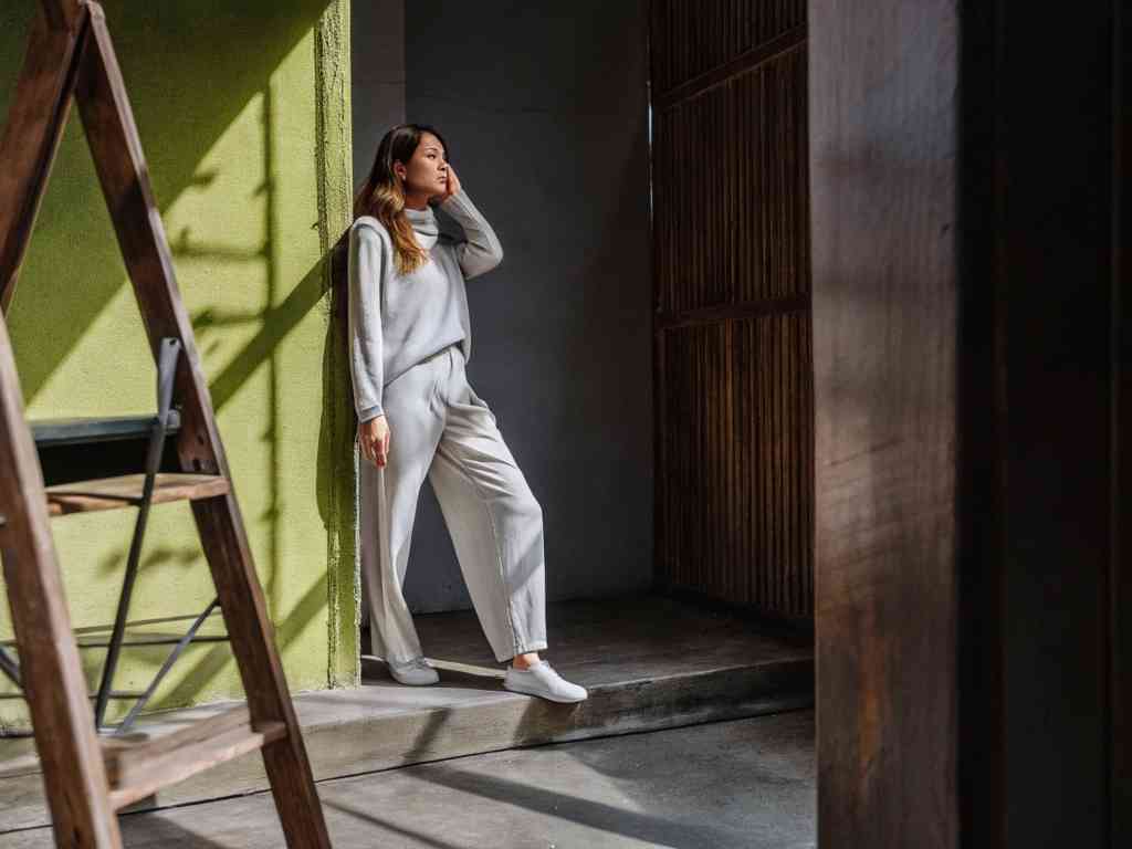Woman in light loungewear leaning on green wall in soft light