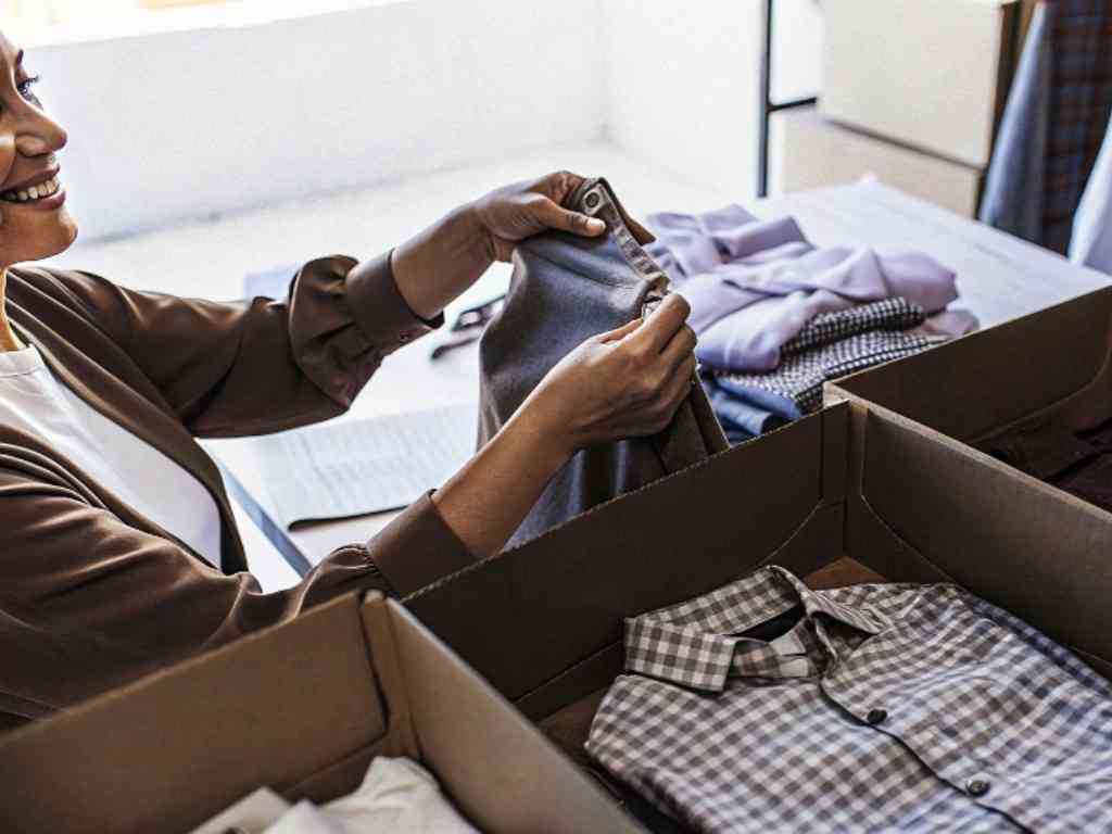 Boutique owner examining a garment from a box filled with folded clothes.