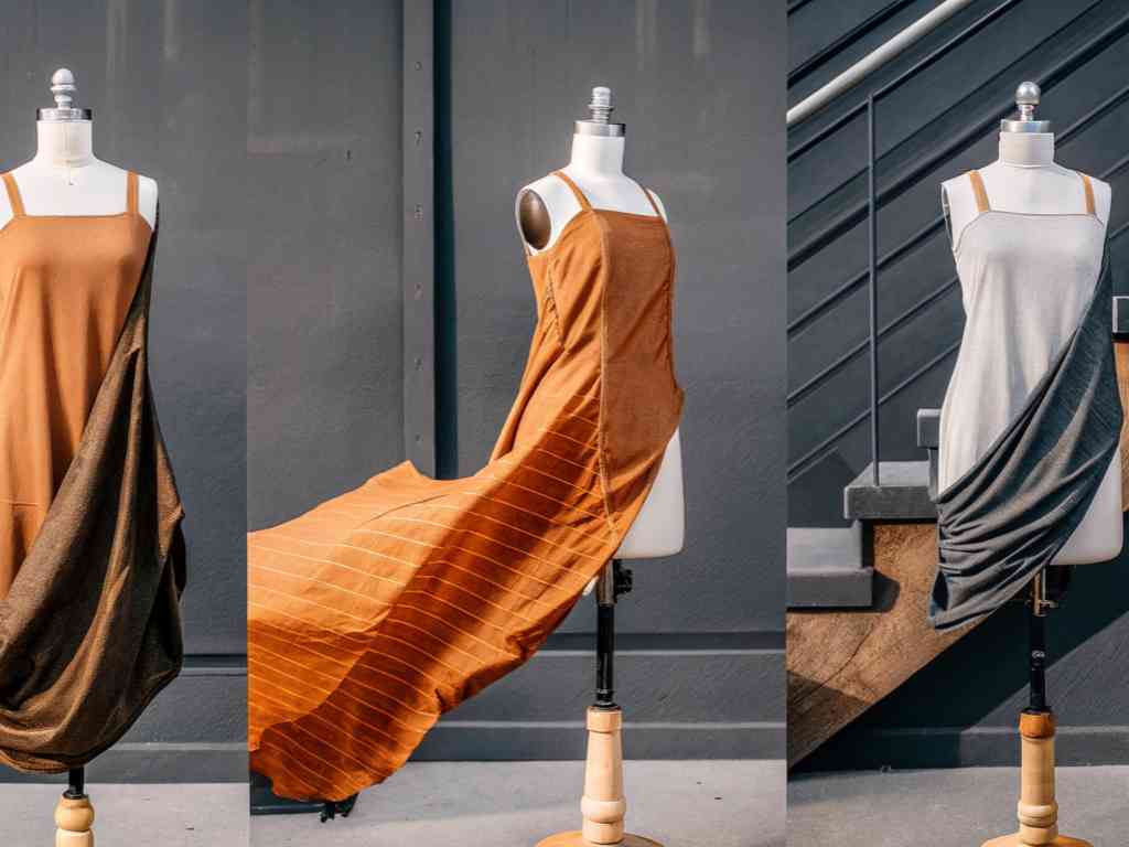 Three mannequins wearing different draped dress samples in warm neutral tones.