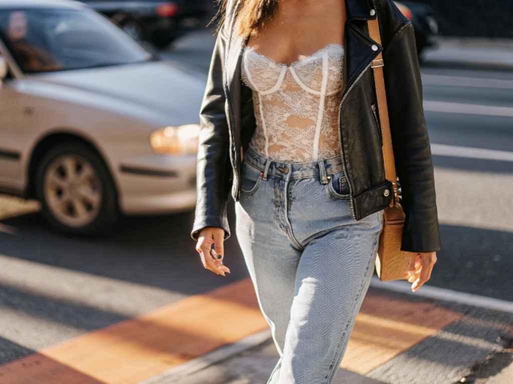 Woman in lace bustier, jeans, and leather jacket crossing street
