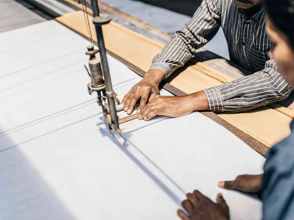 Textile workers guiding fabric through a large industrial cutting machine.