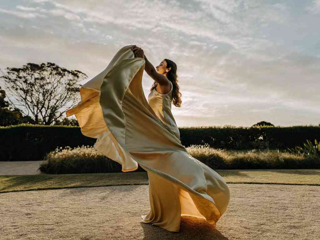 Woman in flowing golden dress twirling outdoors at sunset.
