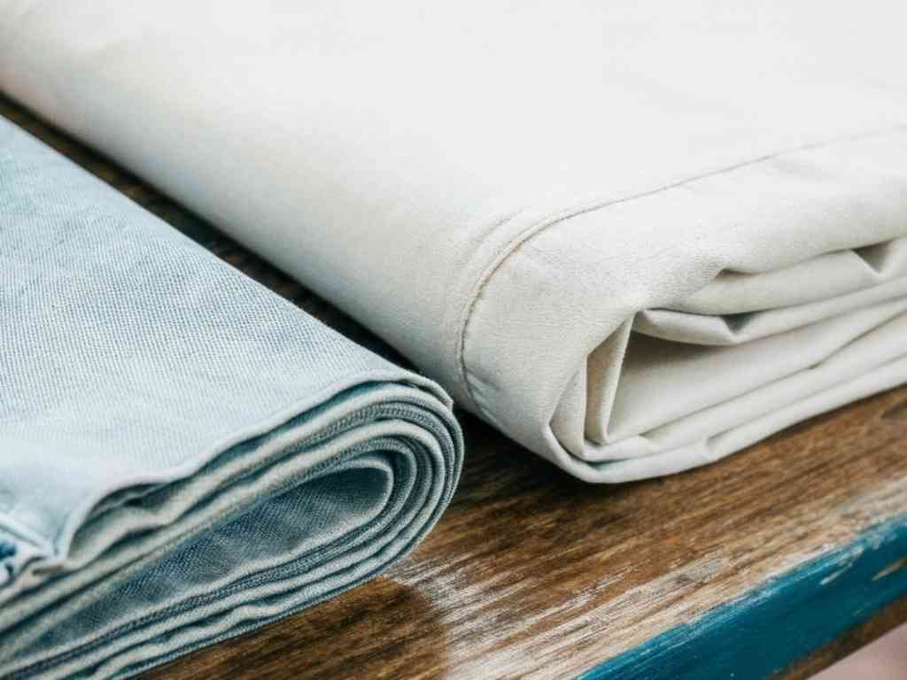 Close-up of rolled denim and cream-colored fabric laid on a wooden surface.