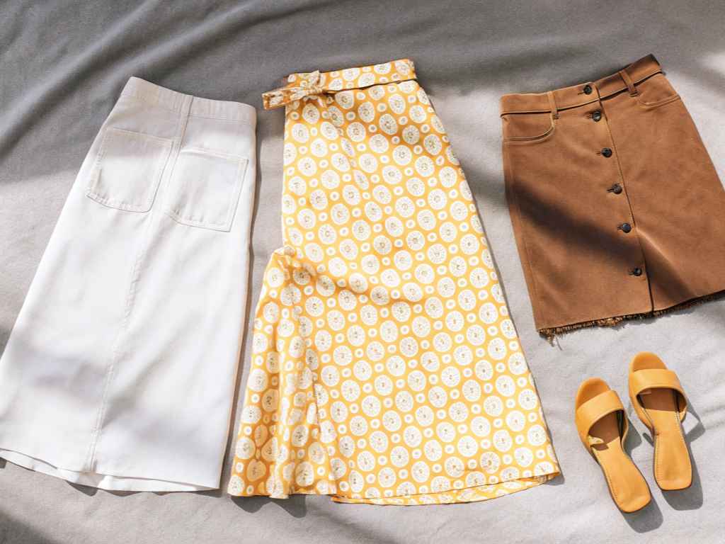 Flat lay of midi skirts and sandals on neutral fabric.