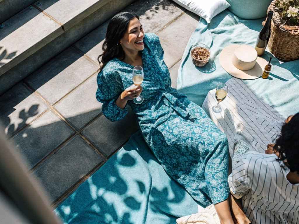 Woman in teal floral dress enjoying wine on picnic blanket