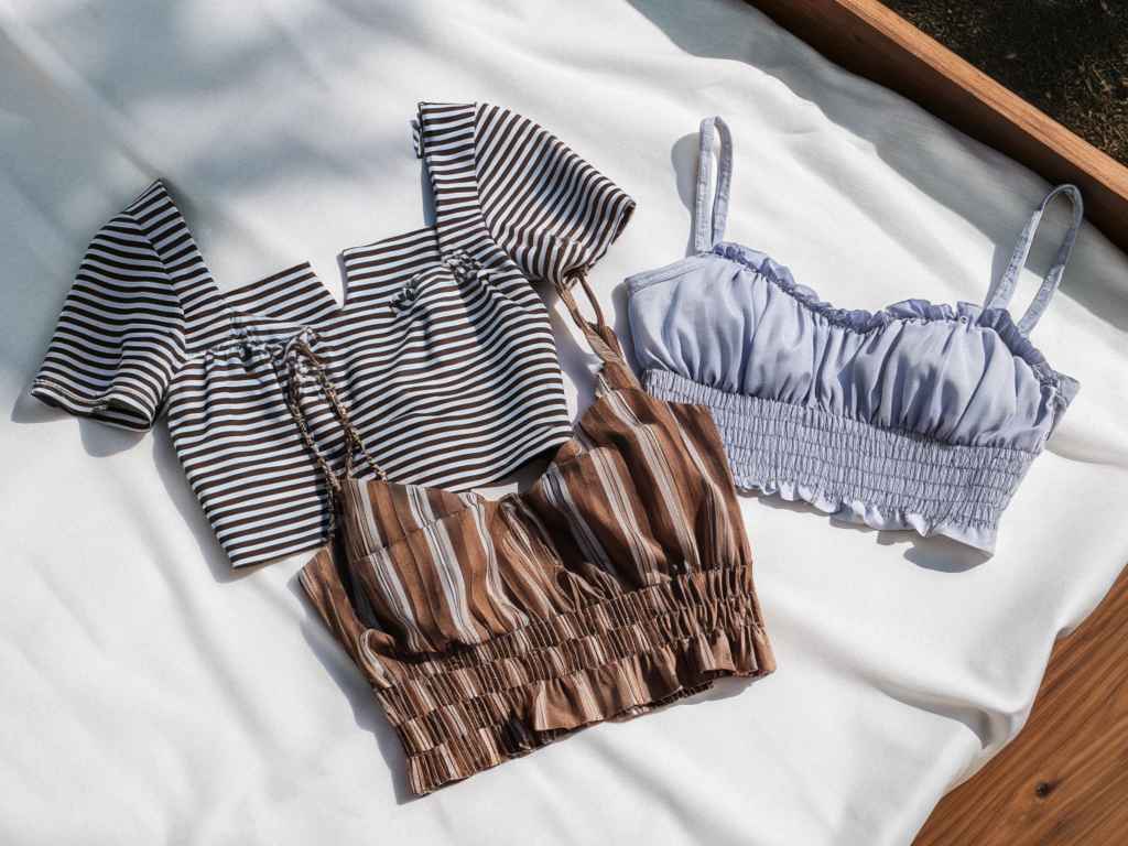 Flat lay of striped and ruched crop tops on linen.