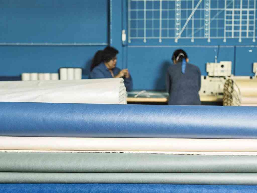 Fabric rolls stacked with two workers behind in a textile studio.