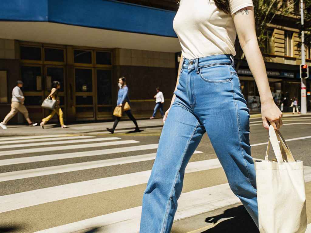 Woman in jeans and white t-shirt crossing city street with tote